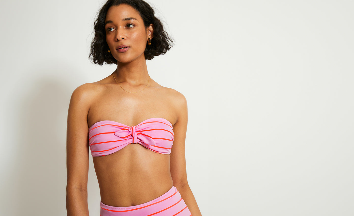 Close up on a woman upper body, she is wearing a lemlem bikini bandeau top in light pink with think neon pink stripes.