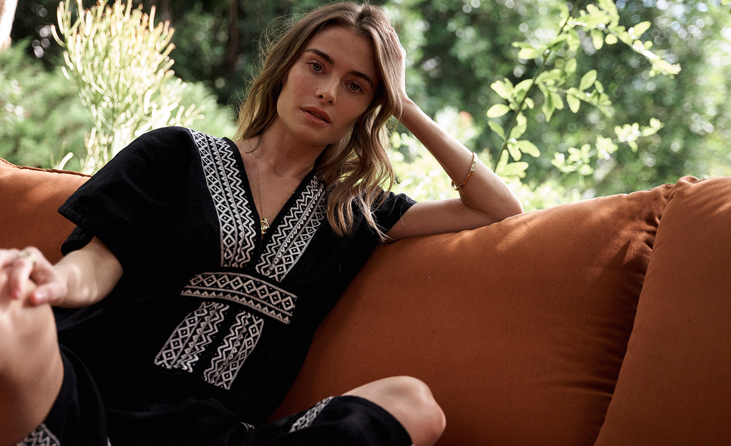 Woman Sitting on the couch in a tree house wearing lemlem Gasira Caftan Featuring white tibeb pattern on black background