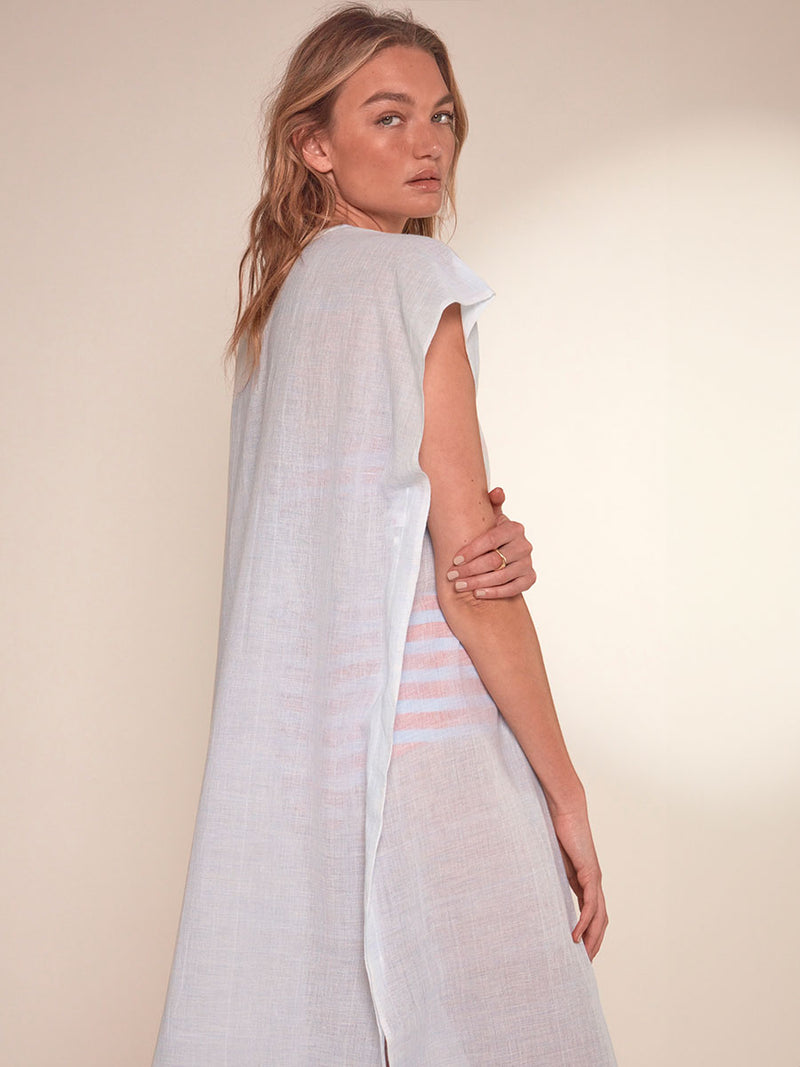 Side View of a Woman Standing Wearing lemlem Dalila V Neck Caftan featuring airy gauze fabric in a delicate pale blue color, jeliba tangerine bandeau top and high waist bottom