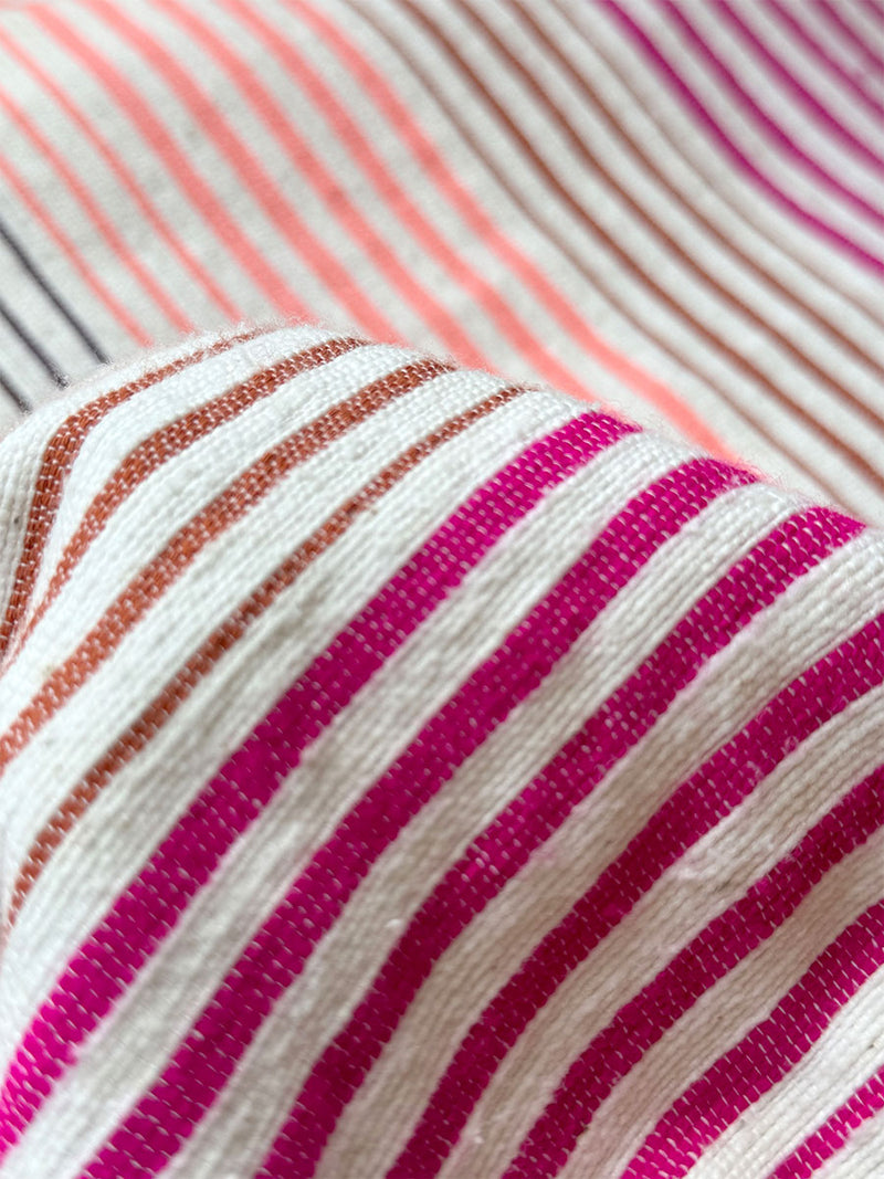 Close up on lemlem Enjori Plum Fabric featuring ombre stripe pattern, where deep plum seamlessly transitions into peach, chestnut, and bright pink