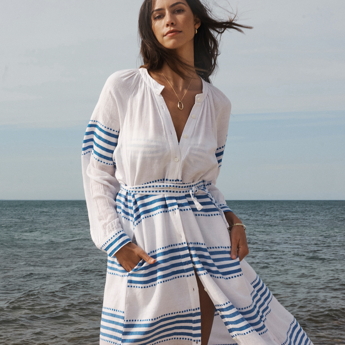 Woman standing on the beach wearing a long white and blue lemlem dress.