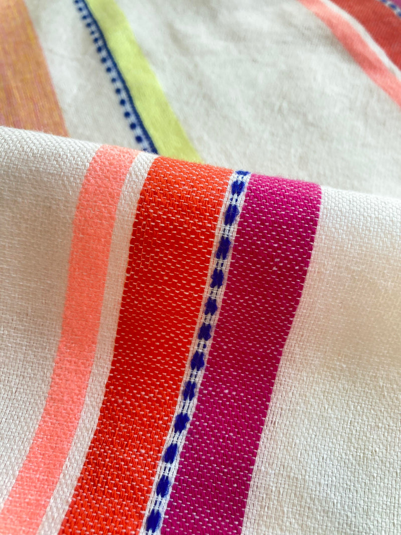 Close up on lemlem Tizita Fabric featuring tibeb inspired stripes in a vibrant fiesta of colors against a creamy vanilla background.