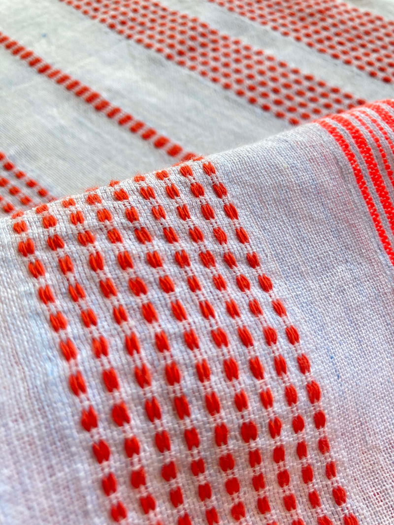 Close up on lemlem tiki skypop fabric featuring playful pattern of red dots becoming stripes on a pale blue background.