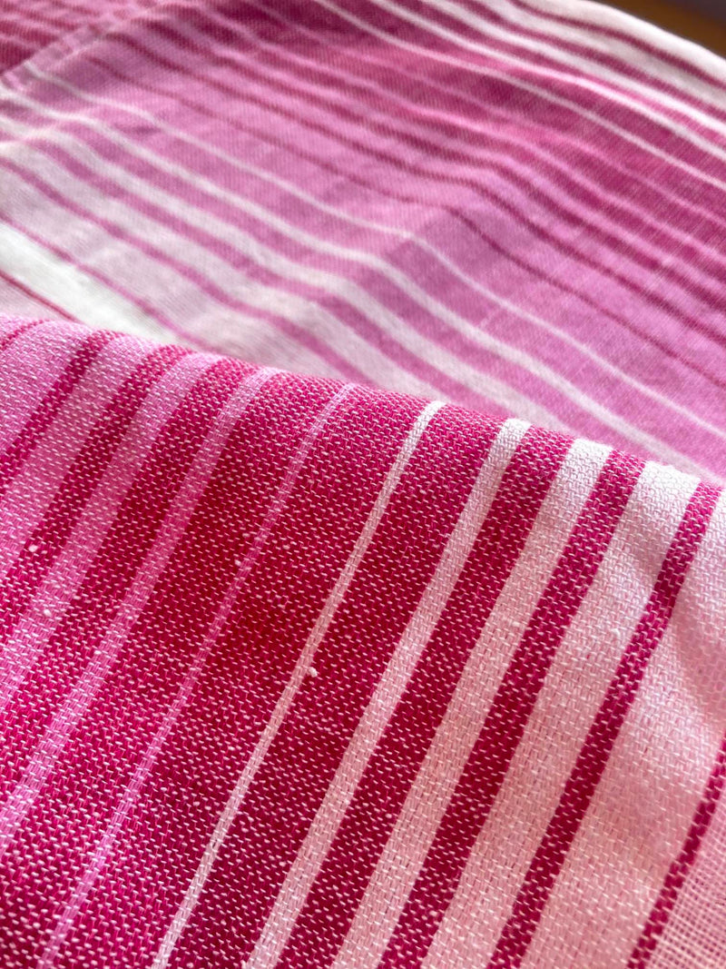 Close up on lemlem Feven Fuchsia Fabric featuring white, soft pink, and raspberry stripes that effortlessly blend into a stunning ombre effect