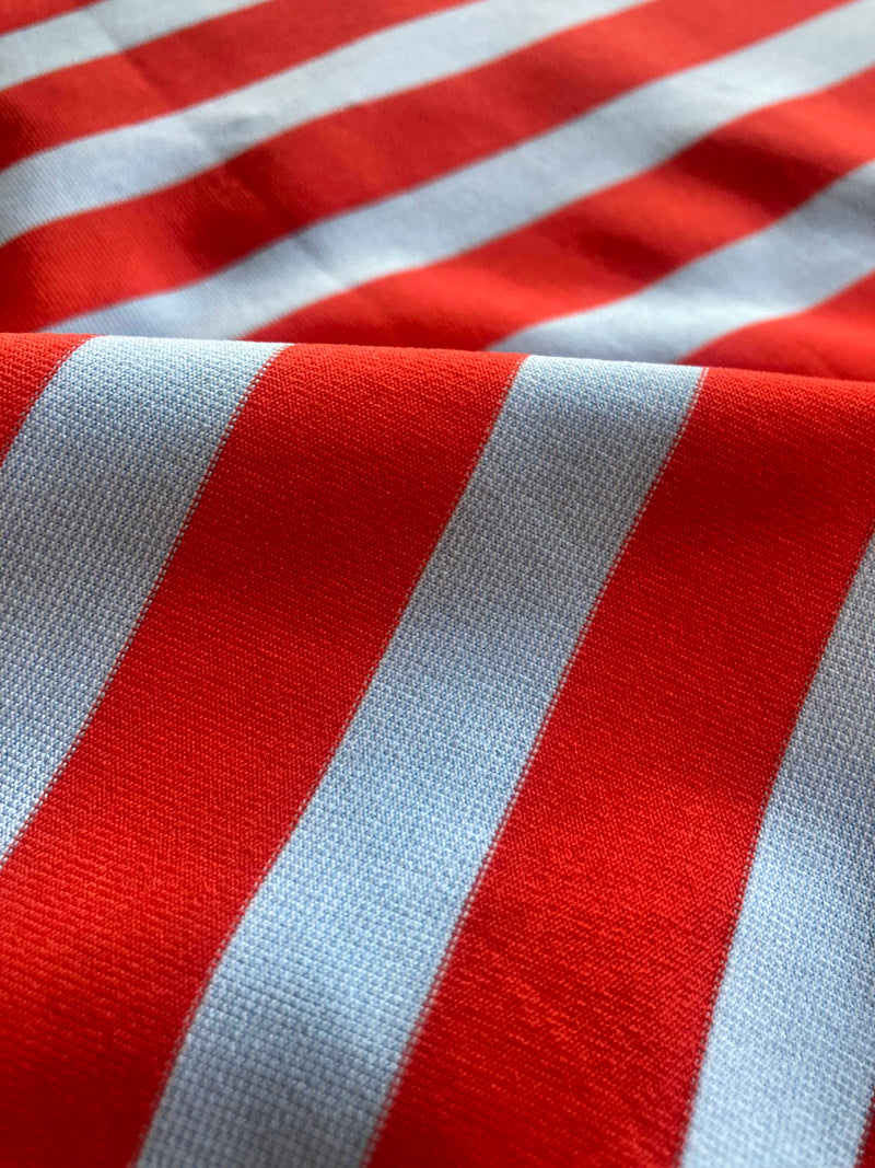 Close up on lemlem Chireti Tangerine fabric featuring bold and bright tangerine color, accented by pale blue stripes