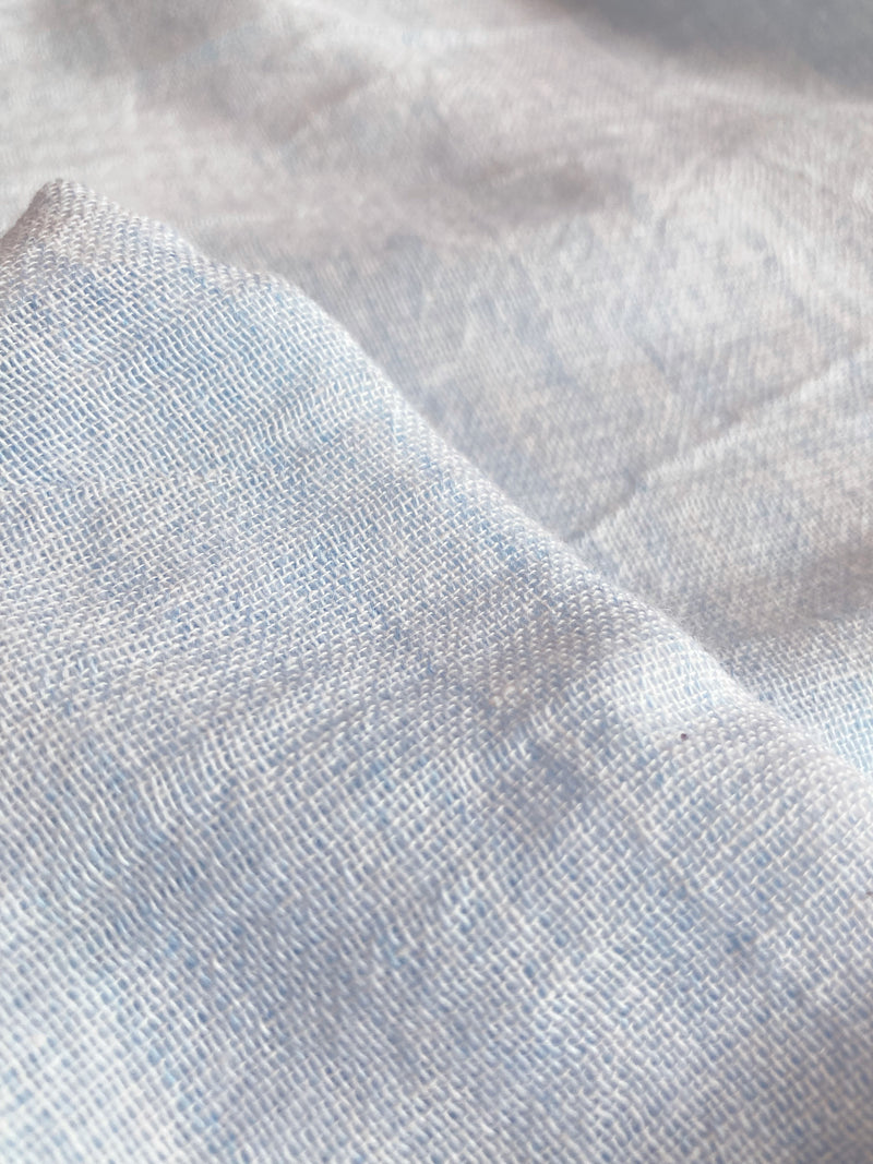 Close up on lemlem Nefas Sky airy gauze fabric in a delicate pale blue color.