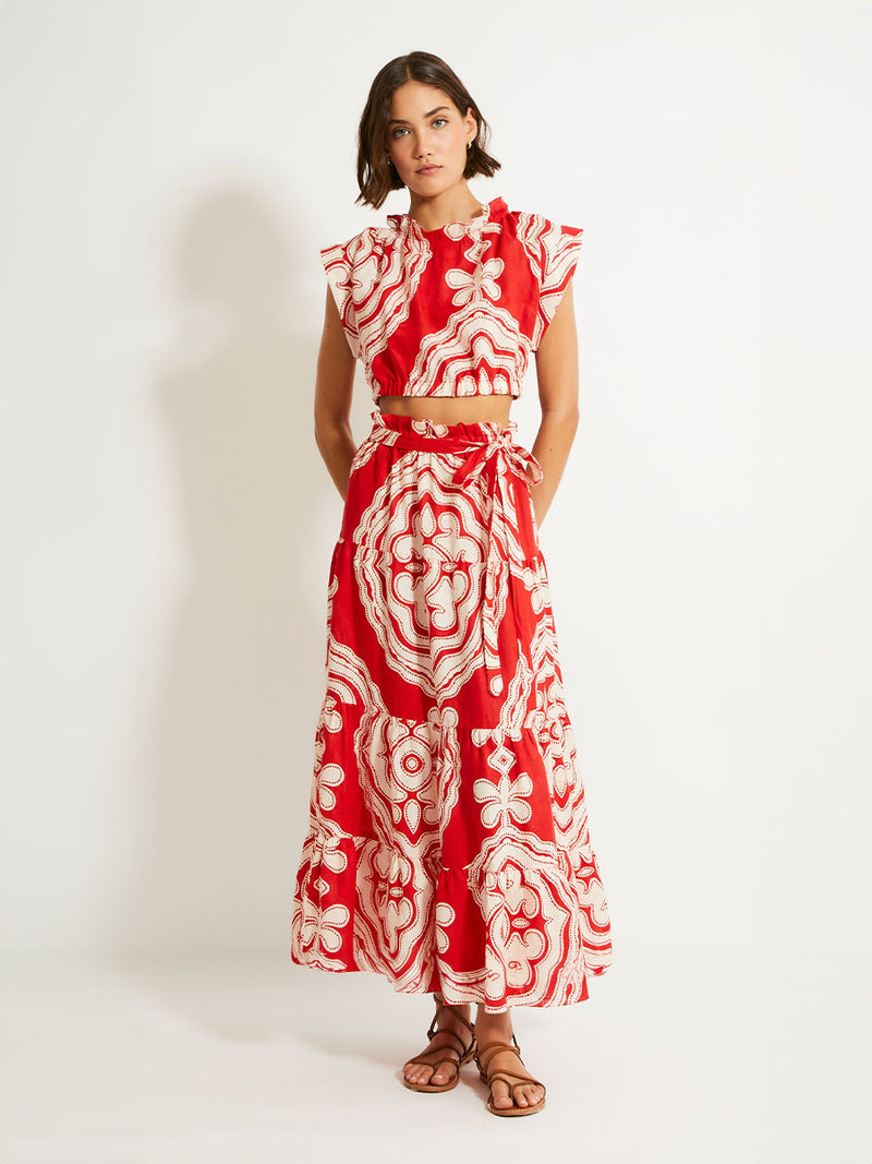 Woman Standing Wearing lemlem MUNA Crop Top and SANA Skirt featuring custom-designed print inspired by ancient architectural patterns in rich, vibrant red and creamy ivory colors.