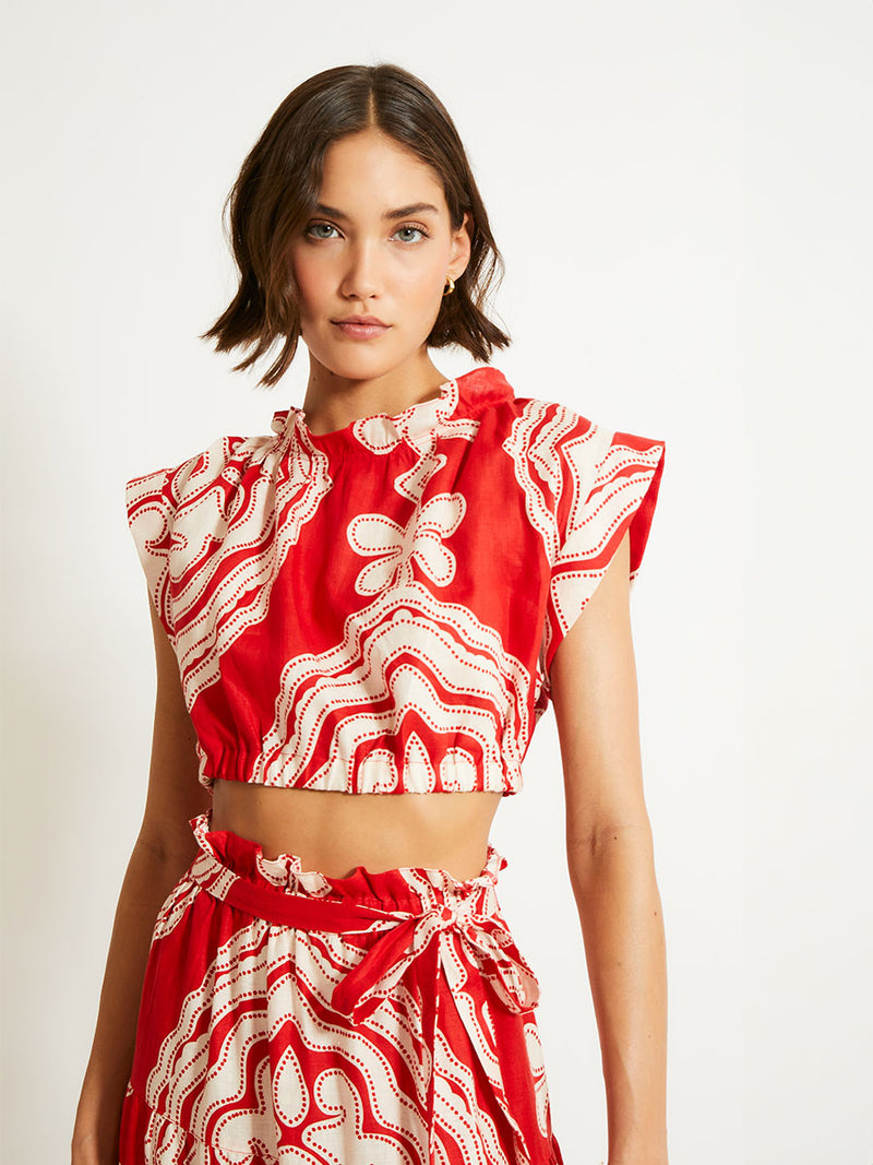 Close up on a Woman Standing Wearing lemlem MUNA Crop Top and SANA Skirt featuring custom-designed print inspired by ancient architectural patterns in rich, vibrant red and creamy ivory colors.