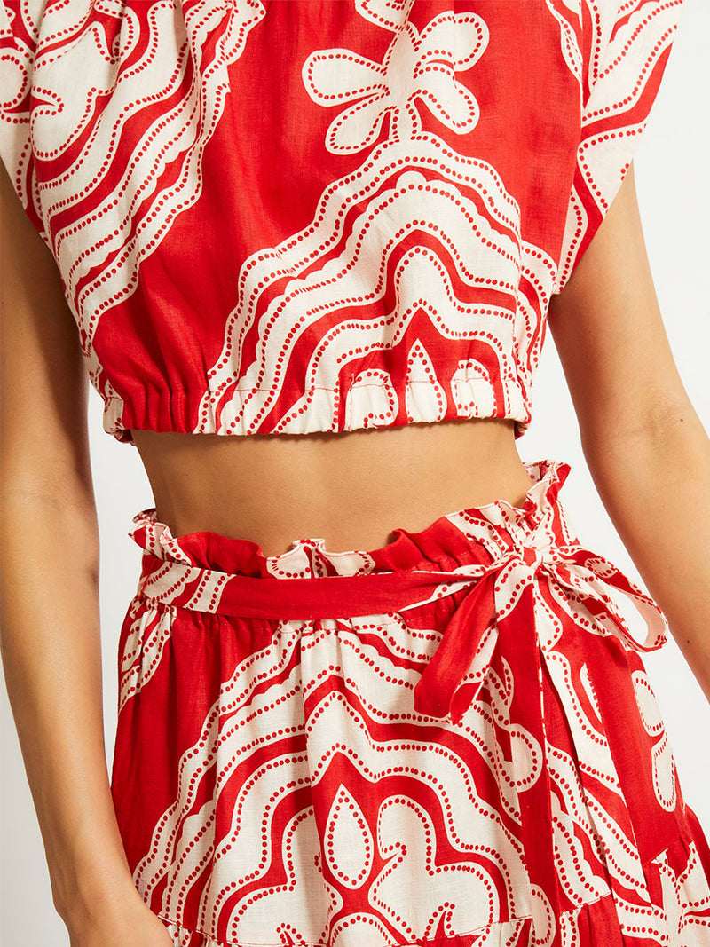 Close up on a Woman Standing Wearing lemlem MUNA Crop Top and SANA Skirt featuring custom-designed print inspired by ancient architectural patterns in rich, vibrant red and creamy ivory colors.