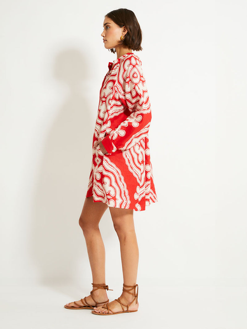 Side of a Woman Standing Wearing lemlem MEAZA Button Up Dress featuring custom-designed print inspired by ancient architectural patterns in rich, vibrant red and creamy ivory colors.