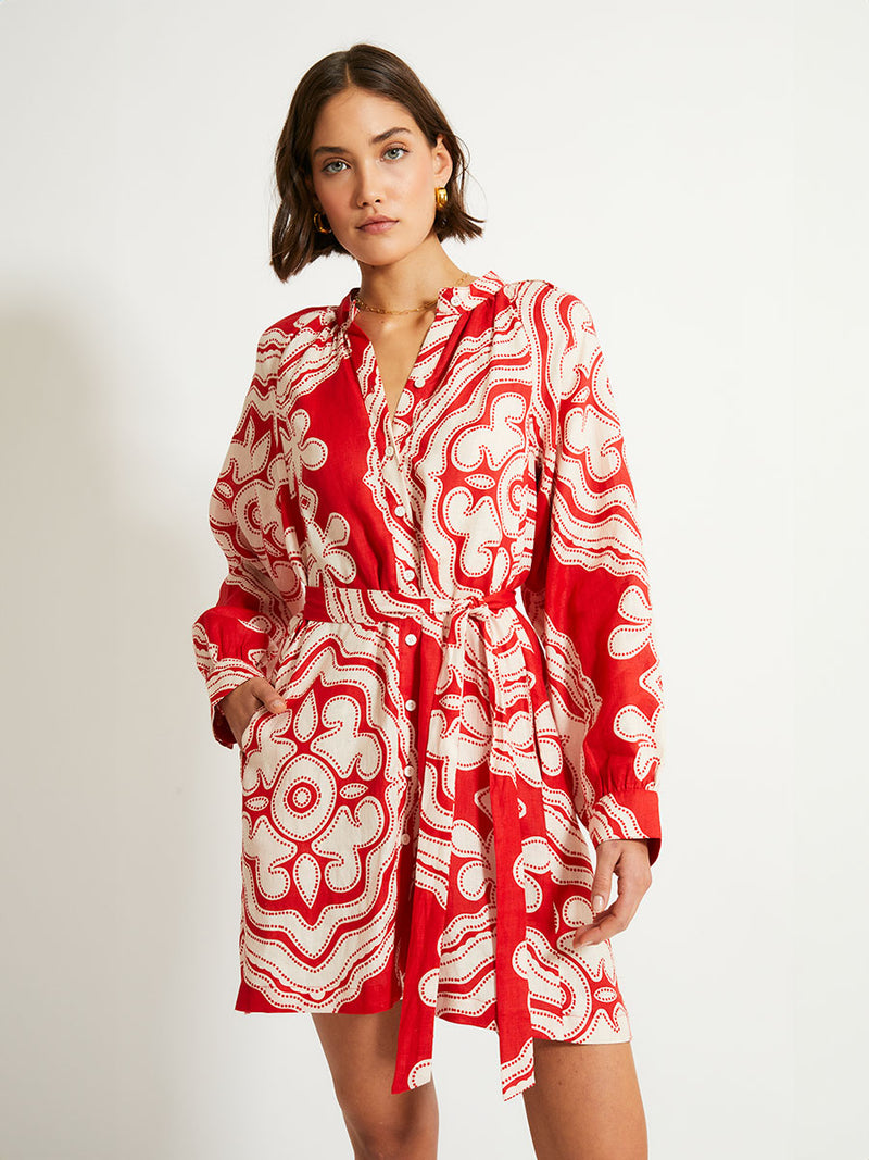 Close up on a Woman Standing Wearing lemlem MEAZA Button Up Dress featuring custom-designed print inspired by ancient architectural patterns in rich, vibrant red and creamy ivory colors.