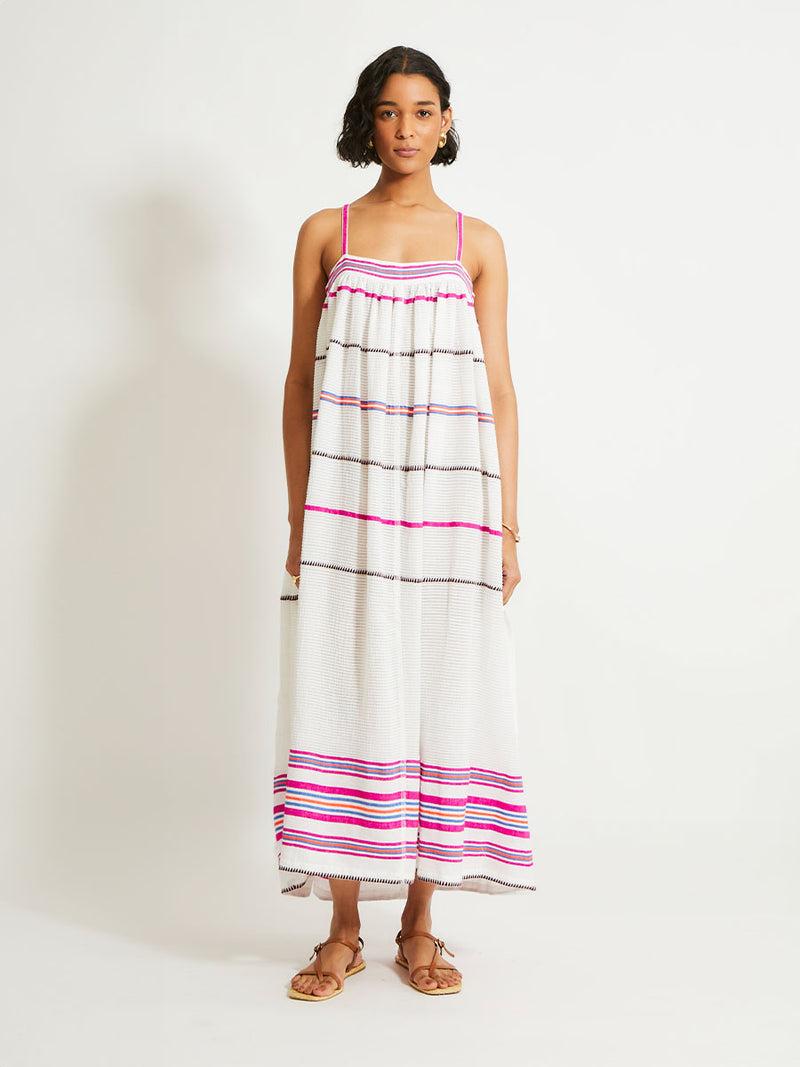 Woman Standing Wearing lemlem Eda Slip Dress featuring a stripe pattern of bright magenta, blue, and orange on s crispy white background. 