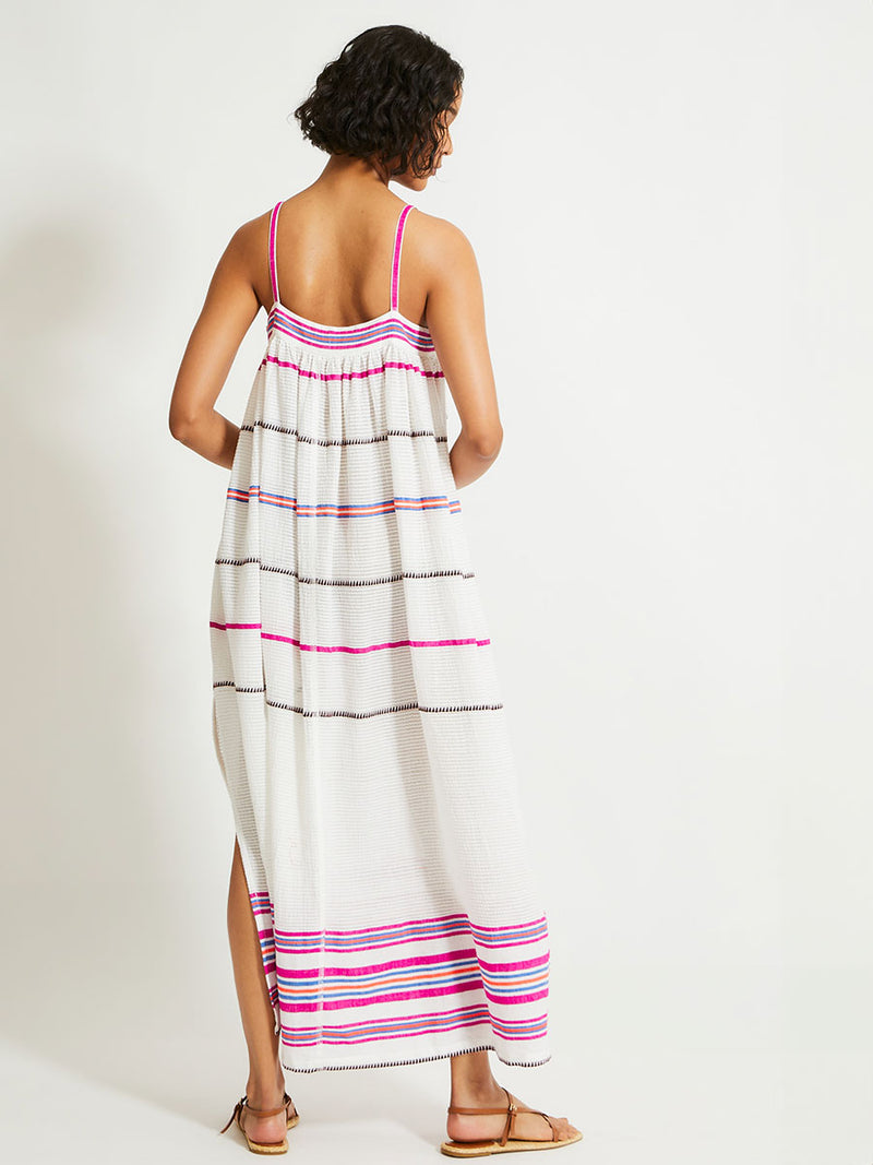 Back of a Woman Standing Wearing lemlem Eda Slip Dress featuring a stripe pattern of bright magenta, blue, and orange on s crispy white background. 