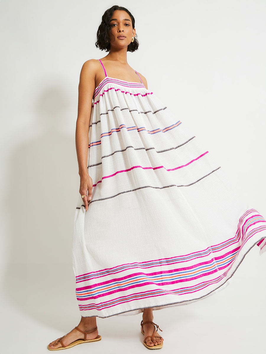 Woman Standing Wearing lemlem Eda Slip Dress featuring a stripe pattern of bright magenta, blue, and orange on s crispy white background. 