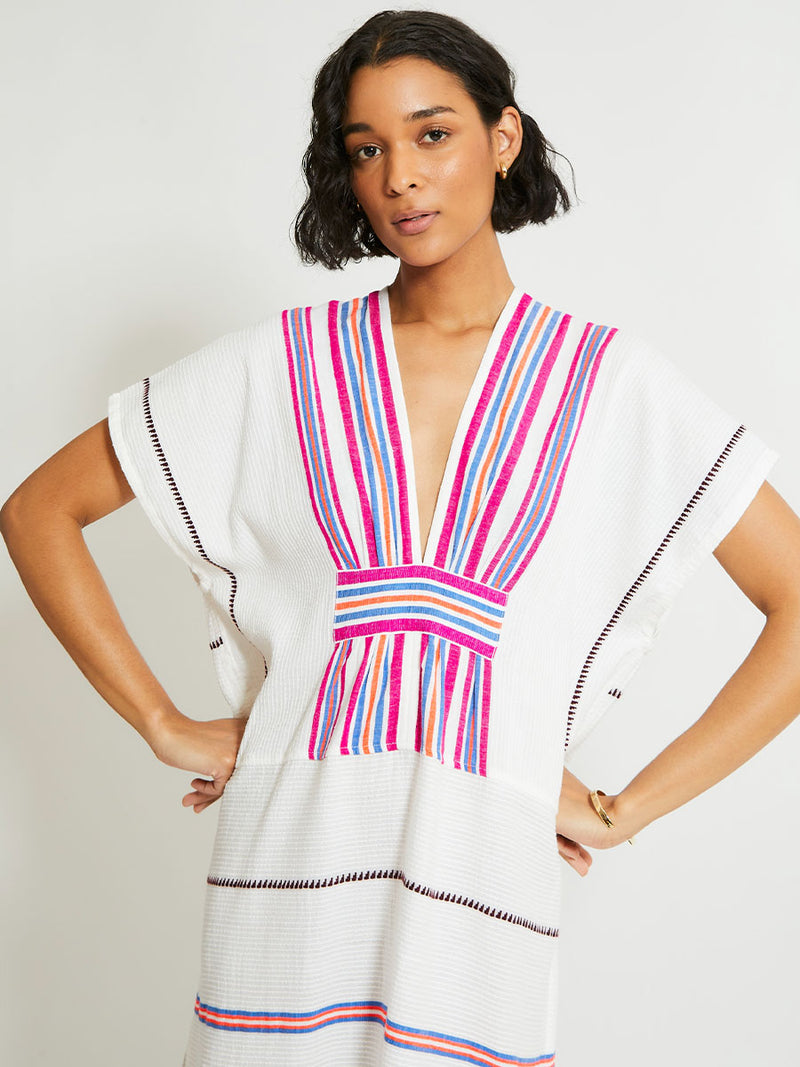 Woman Standing Wearing lemlem Gasira Caftan featuring stripe pattern of bright magenta, blue, and orange on s crispy white background.