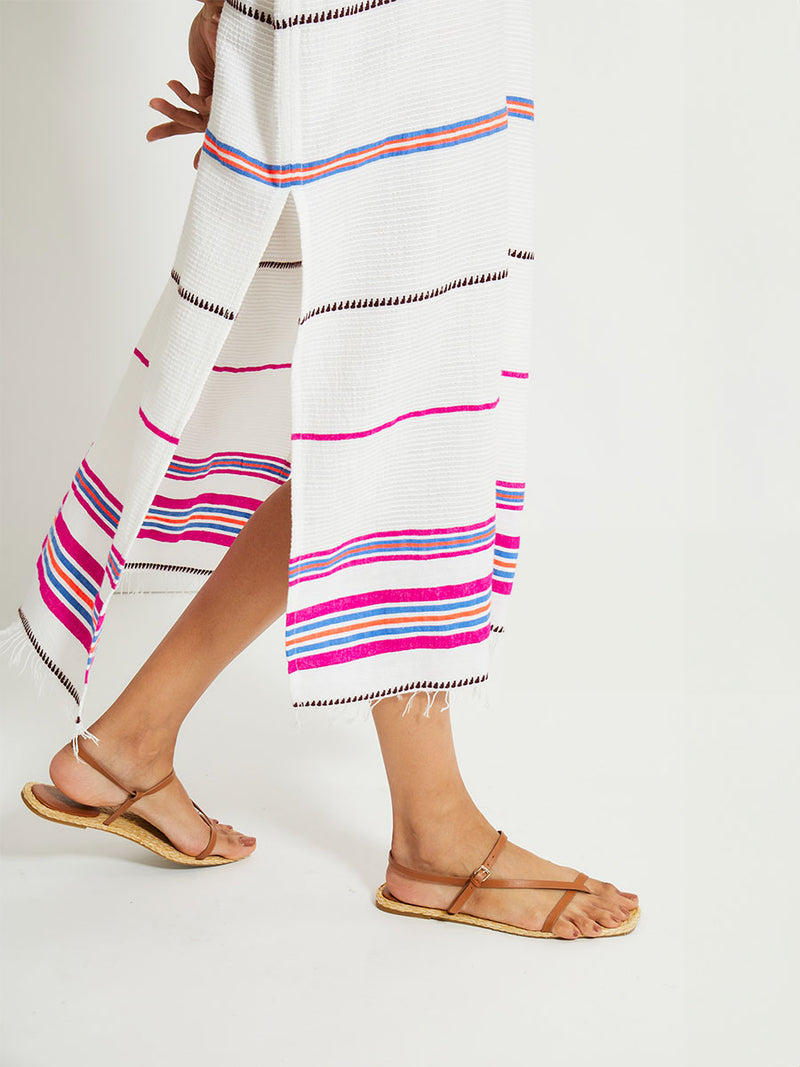 Close up on Woman's legs  Standing Wearing lemlem Gasira Caftan featuring stripe pattern of bright magenta, blue, and orange on s crispy white background.