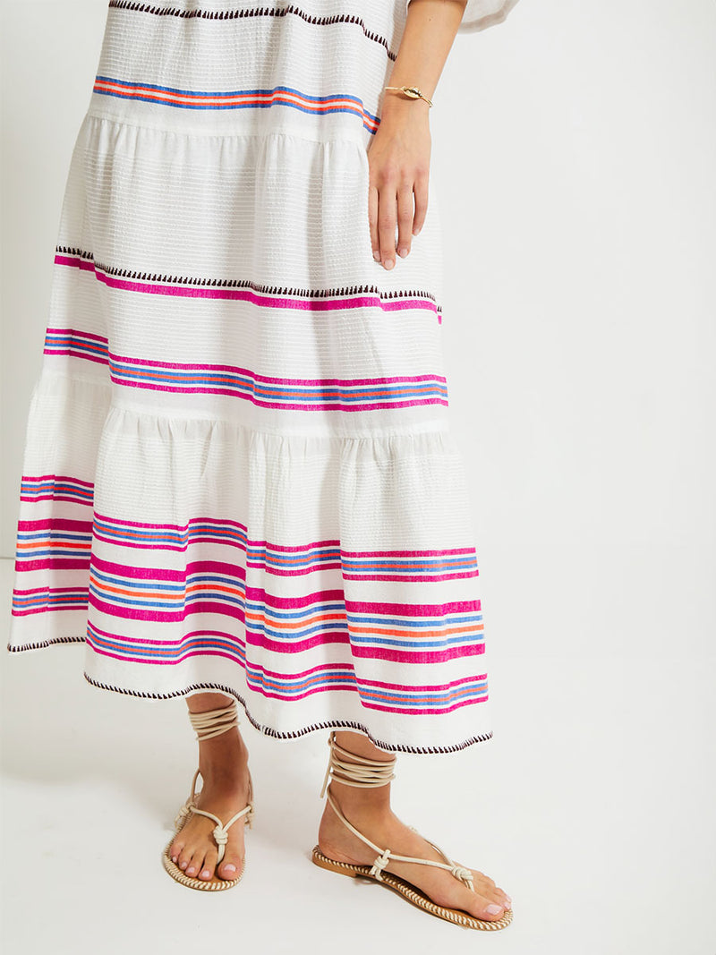 Close up on woman's legs Standing Wearing lemlem HAWI Flutter Dress featuring stripe pattern of bright magenta, blue, and orange on s crispy white background.