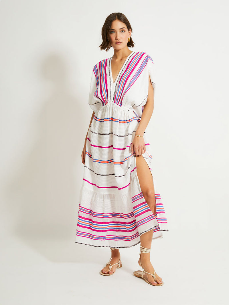 Woman Standing Wearing lemlem Leila Plunge Dress Featuring stripe pattern of bright magenta, blue, and orange on s crispy white background