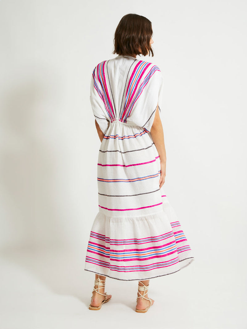 Back of a Woman Standing Wearing lemlem Leila Plunge Dress Featuring stripe pattern of bright magenta, blue, and orange on s crispy white background