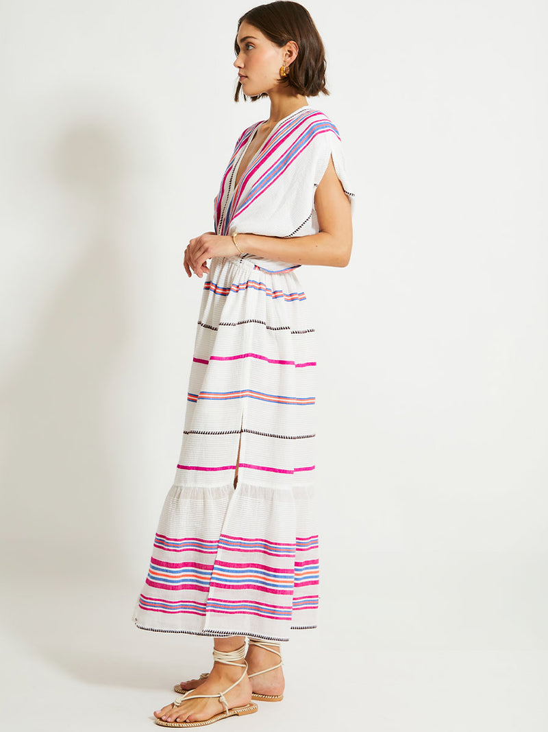 Side View of a Woman Standing Wearing lemlem Leila Plunge Dress Featuring stripe pattern of bright magenta, blue, and orange on s crispy white background