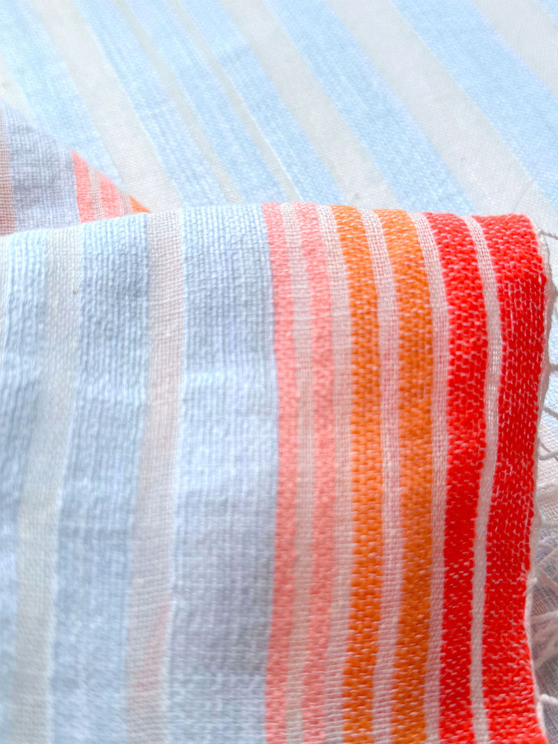 close up on lemlem airi sky fabric featuring soft, variegated two-color stripe in sky blue and cream, complemented by placed bands of bright orange and tangerine.