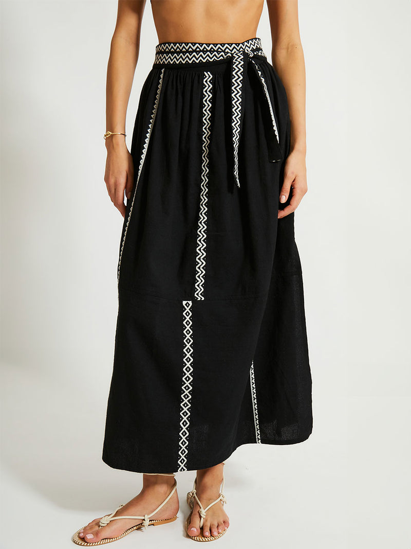 Close up on a Woman Wearing lemlem TOLA Skirt Featuring rich black background with intricate cream Tibeb border pattern