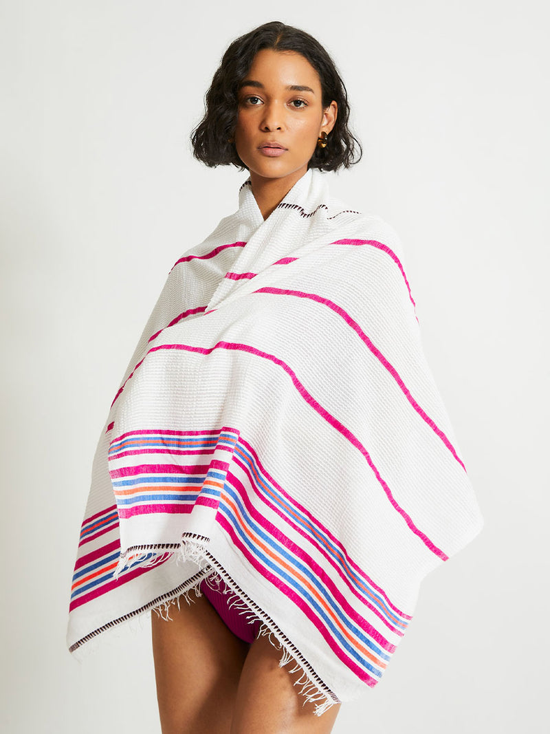 Woman Standing wrapped in lemlem LEMA Sarong featuring stripe pattern of bright magenta, blue, and orange on s crispy white background 