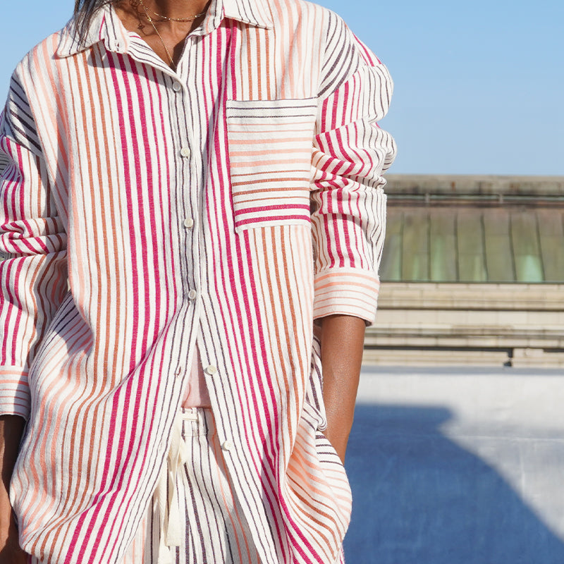 Liya Kebede standing on a New York city roof wearing the new lemlem Mariam shirt and matching pants in white with thin pink and orange stripes.