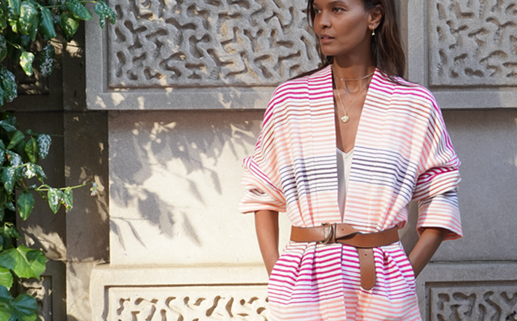 Liya Kebede standing in front of a wall wearing the new lemlem Terara jacket in white with thin pink and orange stripes.