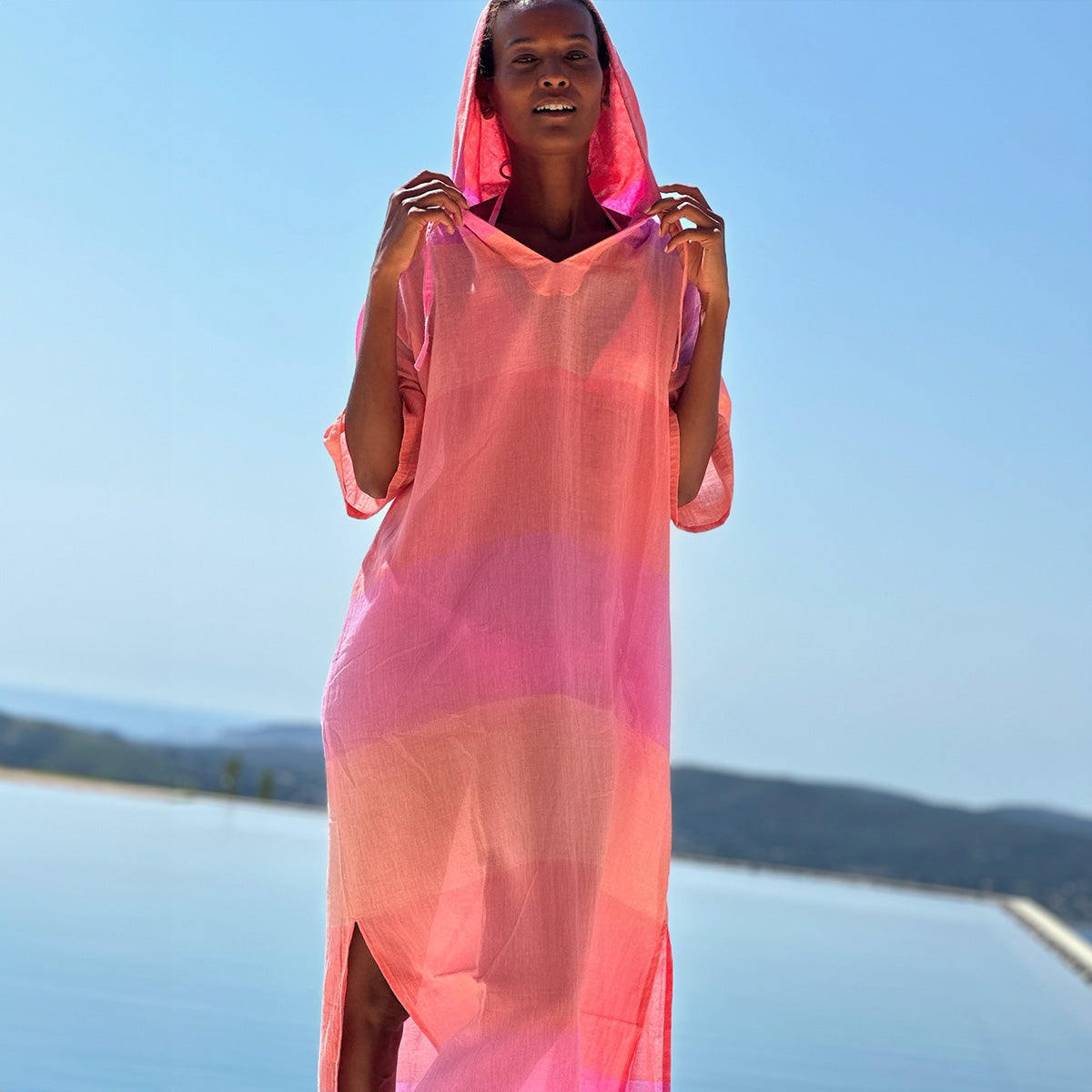 Liya standing by the pool wearing lemlem nefas peach beritu dress featruing color block pattern in orange and pink colors