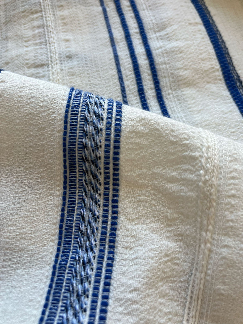 close up on lemlem aberu azure fabric featuring  featuring vertical blue tibeb stripes of varying widths on a white background.