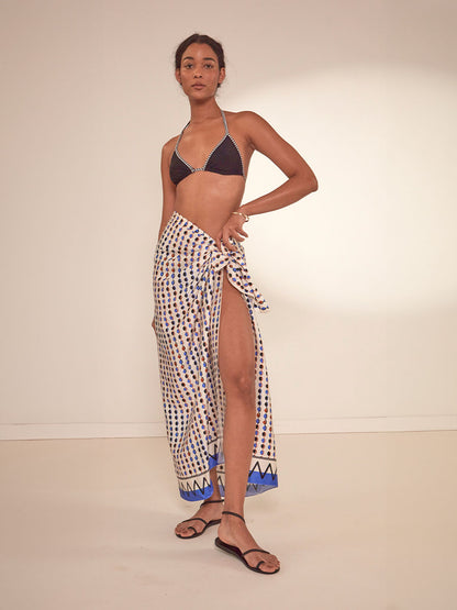 Woman Standing Wearing lemlem Adia Sarong featuring diamond pattern in natural terracotta and rich blue hues against a cream background and lena black triangle top