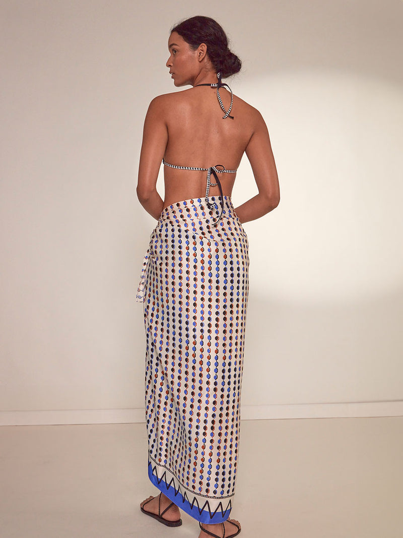 Back View of a Woman Standing Wearing lemlem Adia Sarong featuring diamond pattern in natural terracotta and rich blue hues against a cream background and lena black triangle top