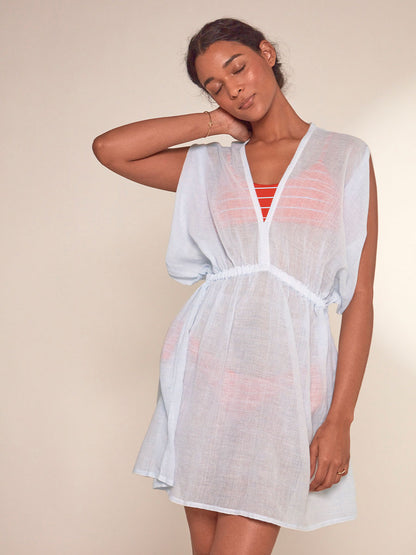 Woman Standing Wearing lemlem Alem Plunge Dress featuring airy gauze fabric in a delicate pale blue color.
