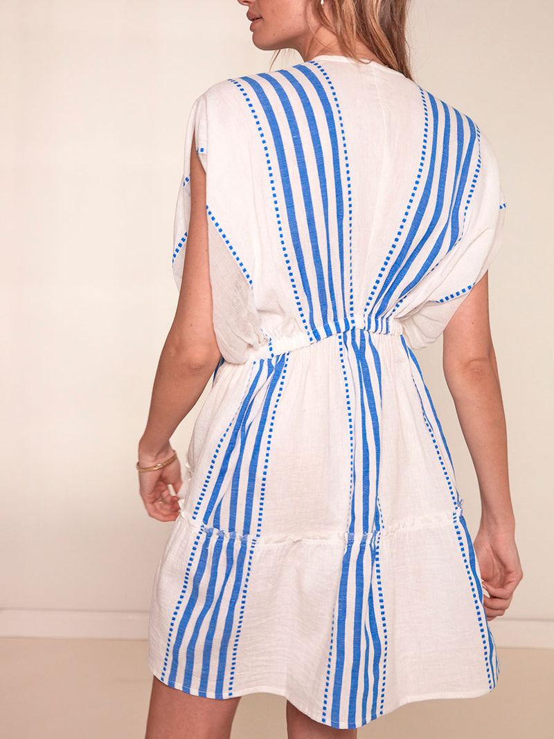 Back View of a Woman Standing Wearing lemlem Alem Plunge Dress Featuring crisp white background and bright blue stripes and dots pattern