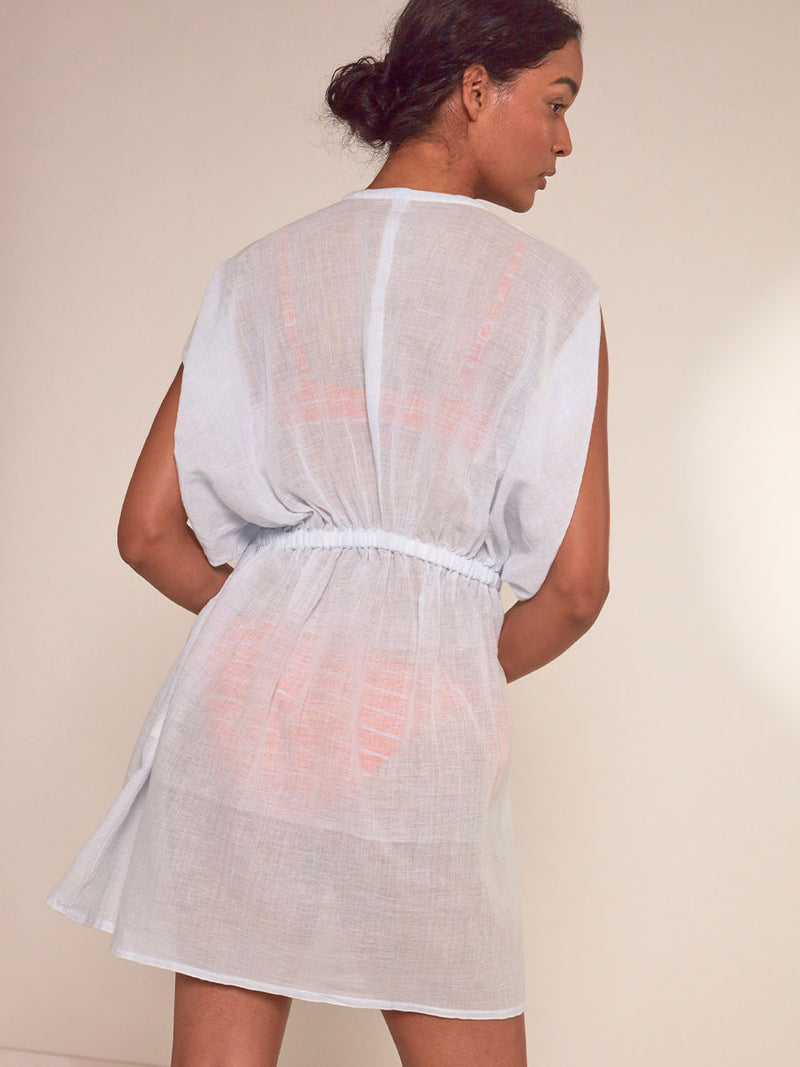 Back View of a  Woman Standing Wearing lemlem Alem Plunge Dress featuring airy gauze fabric in a delicate pale blue color.