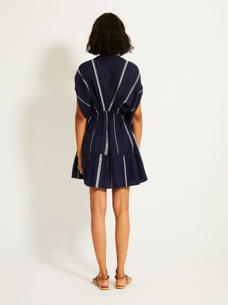 Back view of a woman standing with her hand on her head wearing the Nunu short Plunge Neck in Navy blue with white stripes and graphic lines.