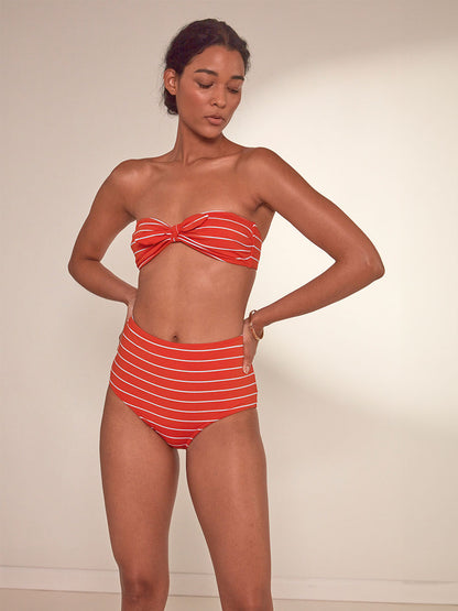 Woman Standing Wearing  lemlem Elsi High Waist Bottom featuring bright juicy tangerine hues accented by pale blue fine stripes and matching bandeau top