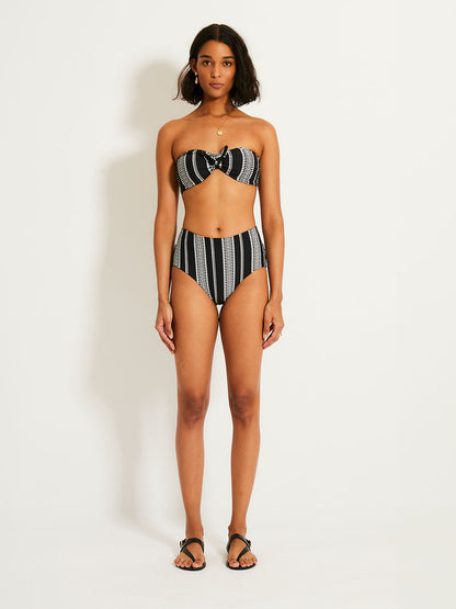 Woman standing wearing the Luchia bandeau bikini top and matching high waist bikini bottom in black with white graphic diamond and arrows.