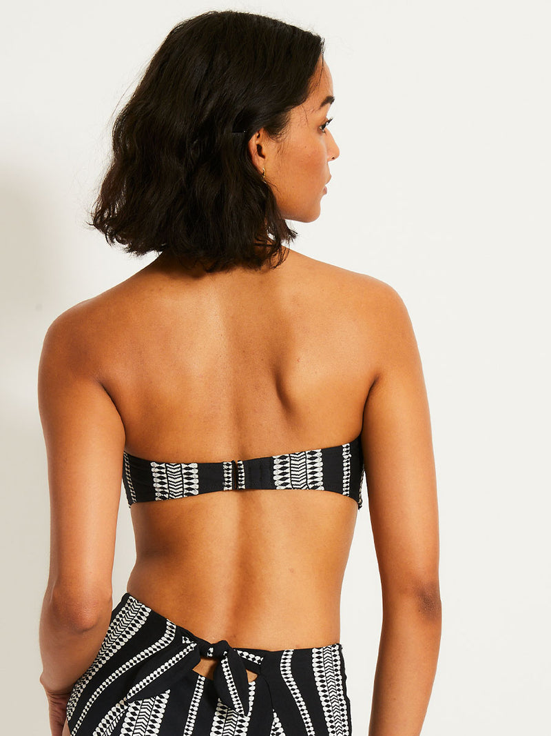 Back of a Woman standing wearing the Luchia Bandeau Top and matching Side Tie Bikini Bottom in black white white graphic diamond and arrows pattern.