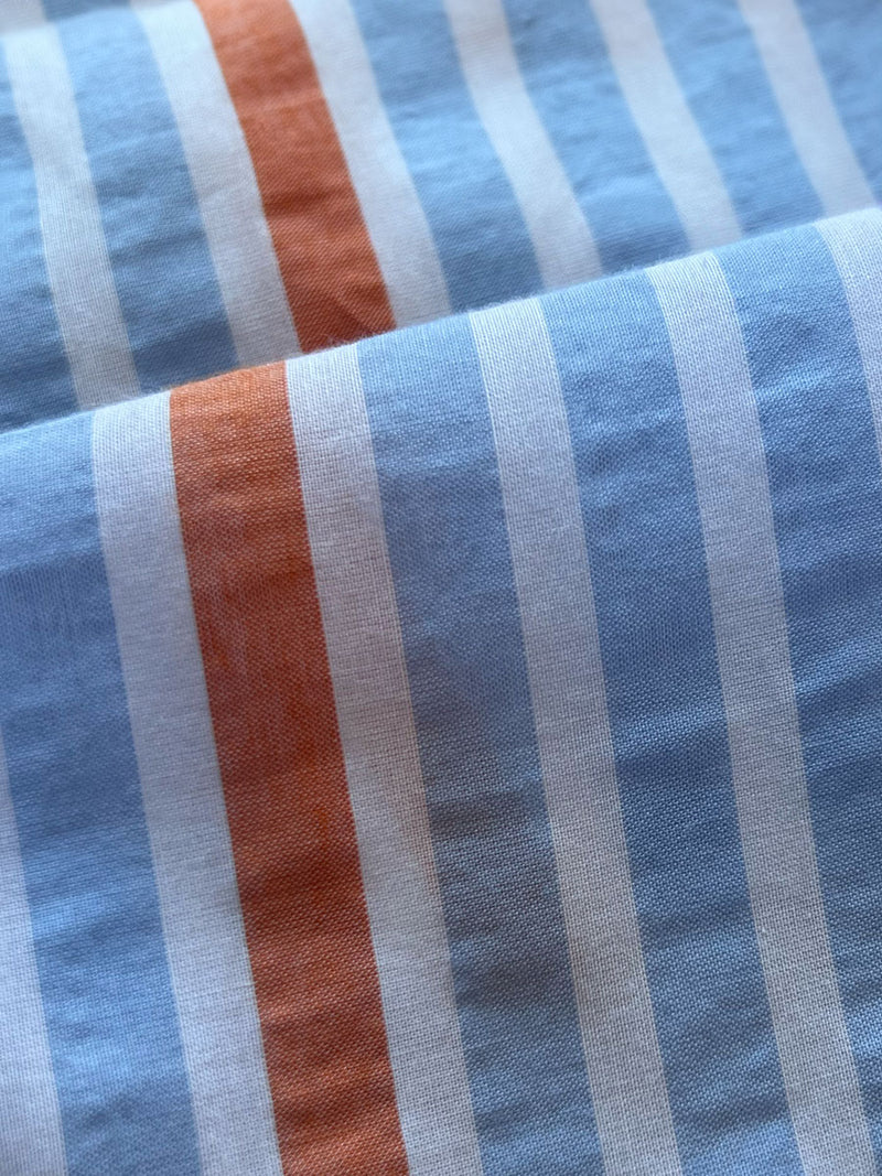 close up on lemlem bahiri blue fabric  featuring airy stripe pattern with pops of orange, lavender and blue