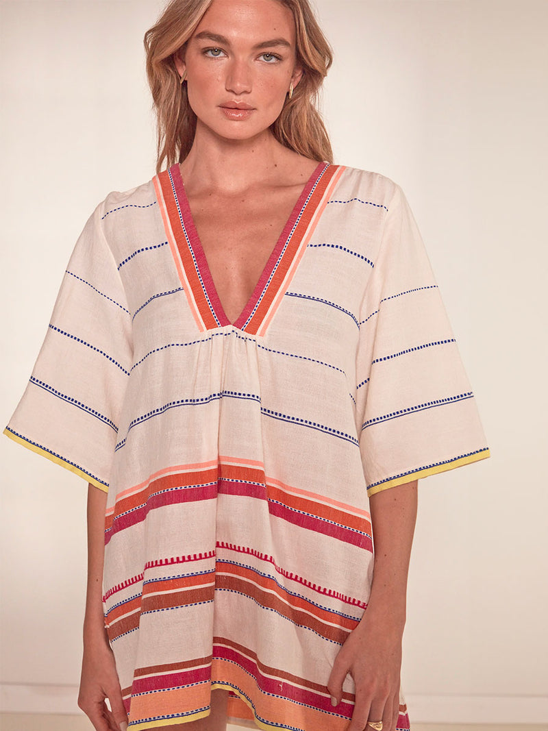 Woman Standing wearing lemlem Belkis Caftan featuring tibeb inspired stripes in a vibrant fiesta of colors against a creamy vanilla background