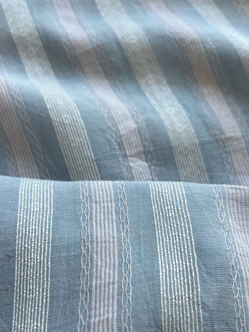 close up on lemlem besu sky fabric featuring elegant light blue hue, gracefully combined in a stripe pattern offering a touch of classic charm and romantic flair.