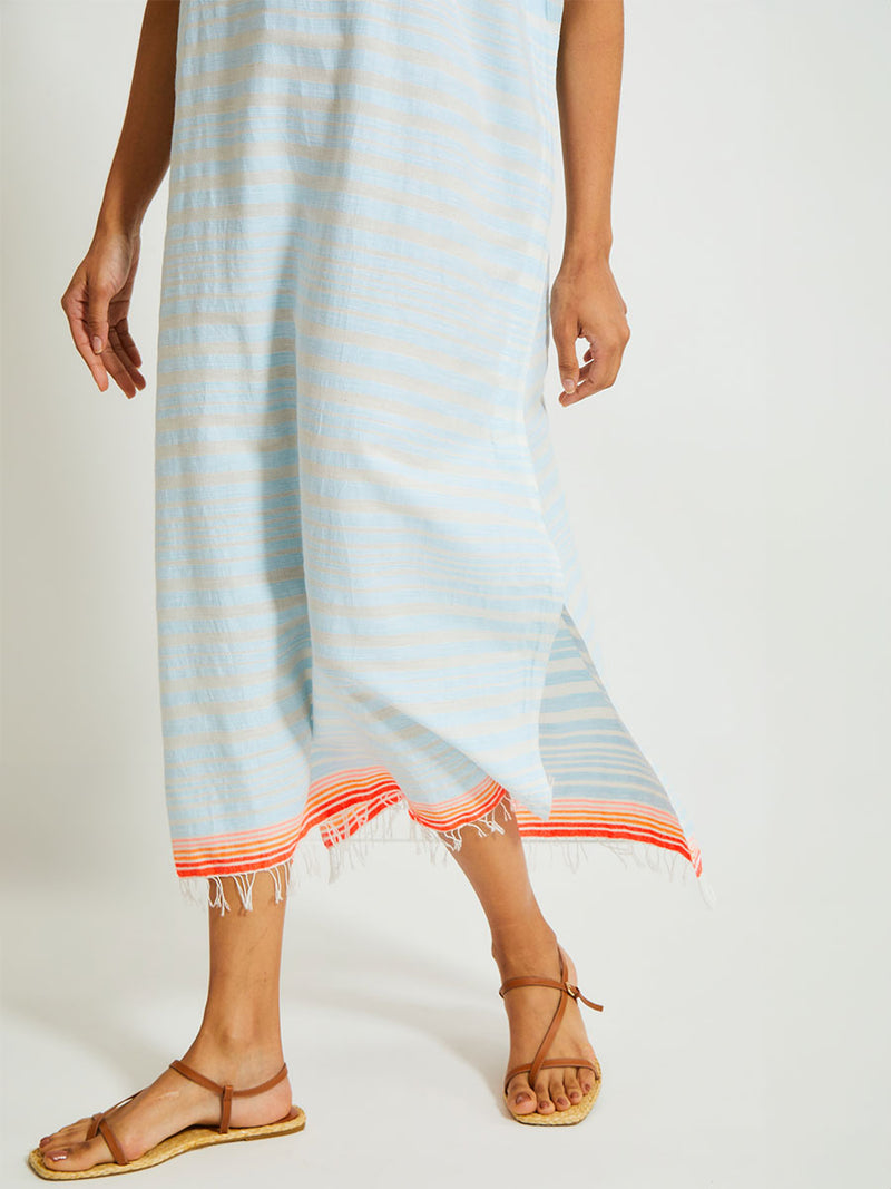 Close up on Woman's legs Standing Wearing lemlem DALILA Caftan featuring a soft, variegated two-color stripe in sky blue and cream, complemented by placed bands of bright orange and tangerine