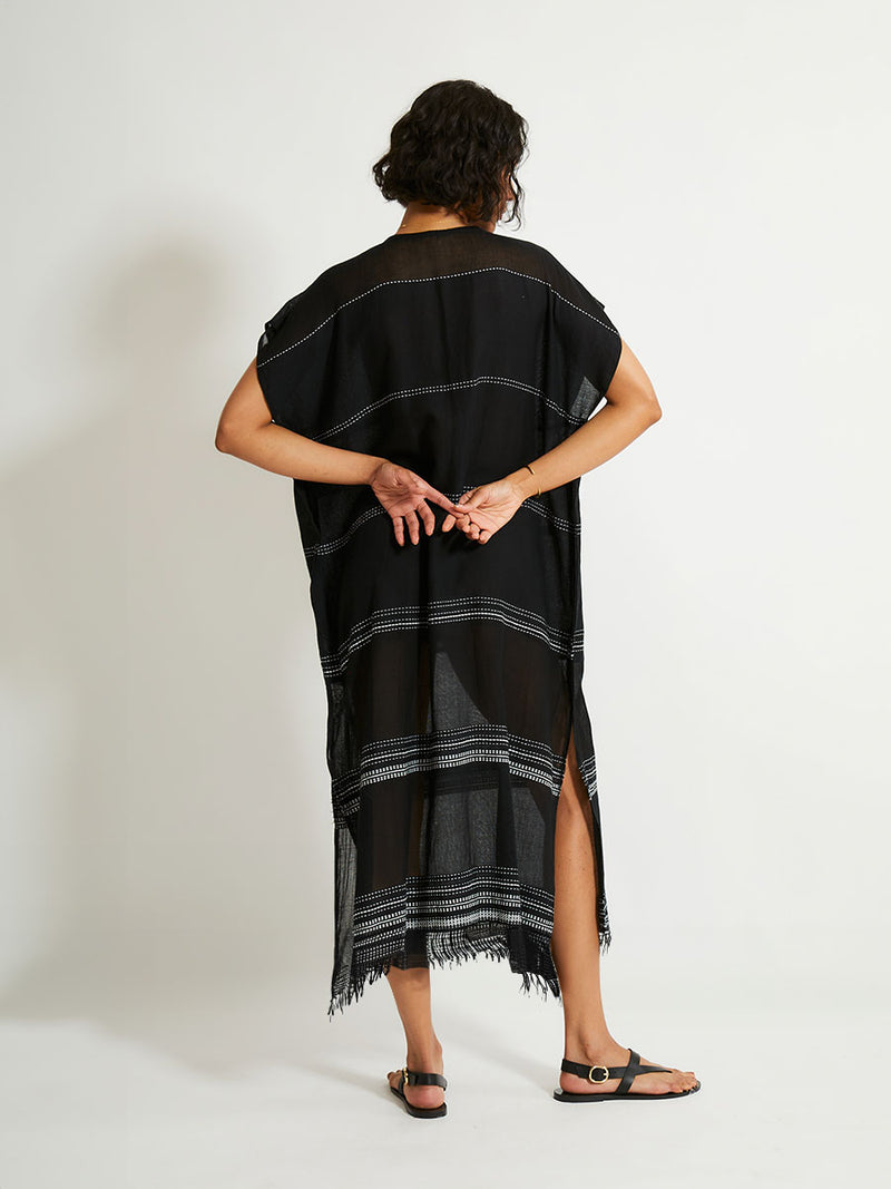 Back of a woman standing wearing the Leliti Classic Caftan in Black with white stitching allover.