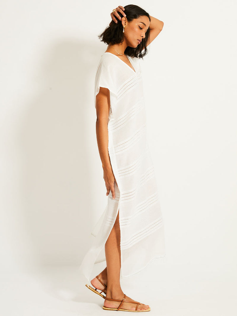 Side view of a woman wearing a white Abira classic caftan with stitches of silver lurex