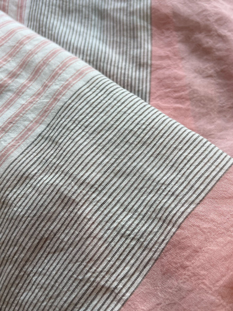 close up on lemlem dera pink fabric featuring beautifully soft palette with a blush pink background and a detailed, silver-grey abstract pattern, exuding a gentle yet sophisticated allure