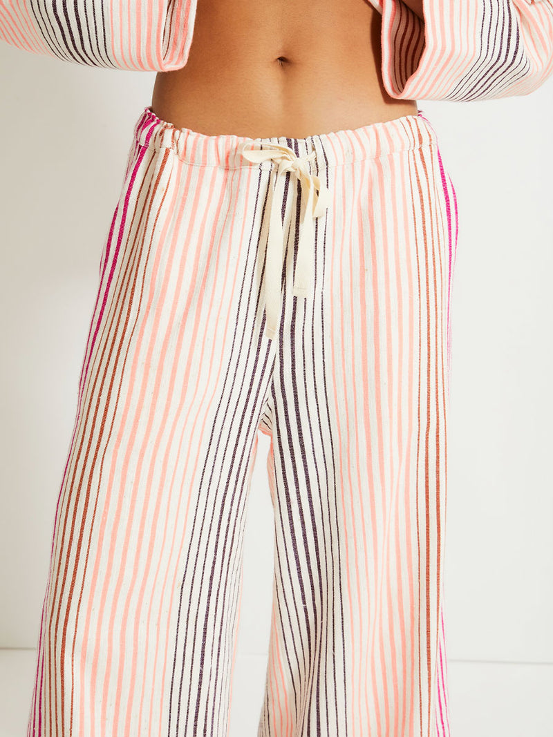 Close up on a Woman Standing Wearing lemlem Terarra Jacket and matching Wide Leg Pants featuring ombre stripe pattern, where deep plum seamlessly transitions into peach, chestnut, and bright pink