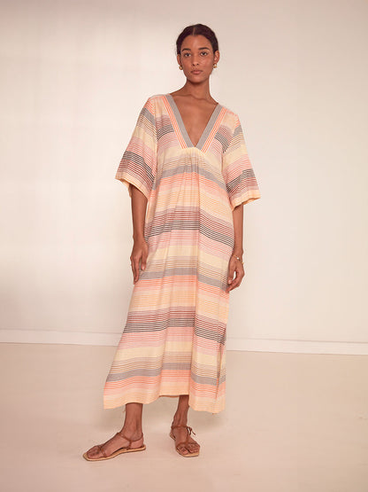 Woman Standing Wearing  lemlem Edna Dress Featuring continuous stripe pattern in warm yellow, orange and peach tones.