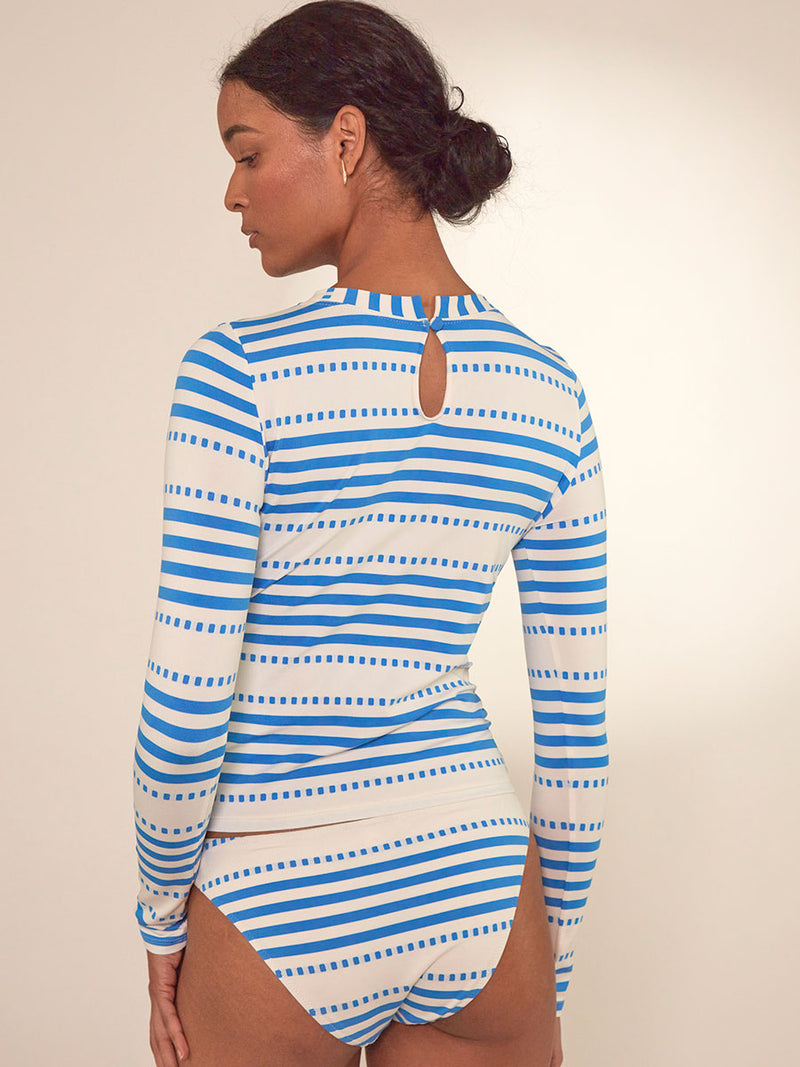 Back Close up on a Woman Standing Wearing lemlem Azeb Rash Guard Featuring crisp white background and bright blue stripes and dots pattern and a matching brief bikini bottom